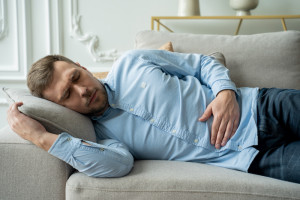 Man suffering from stomach ache while lying on sofa at home. Handsome young man suffering from stomach ache while lying on sofa at home